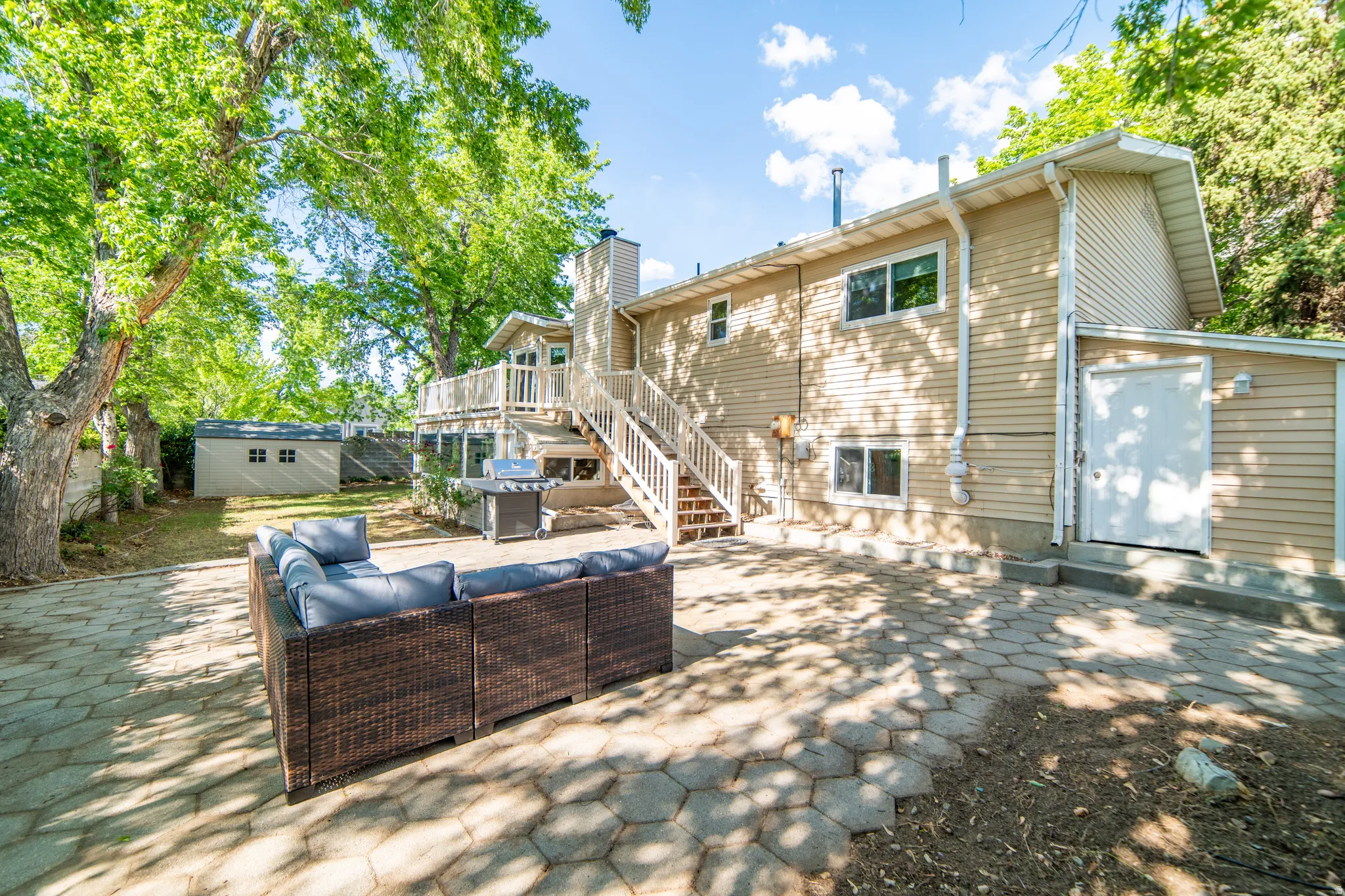 Rear exterior featuring a multi-level deck, lower patio with paver stones, and a detached storage shed