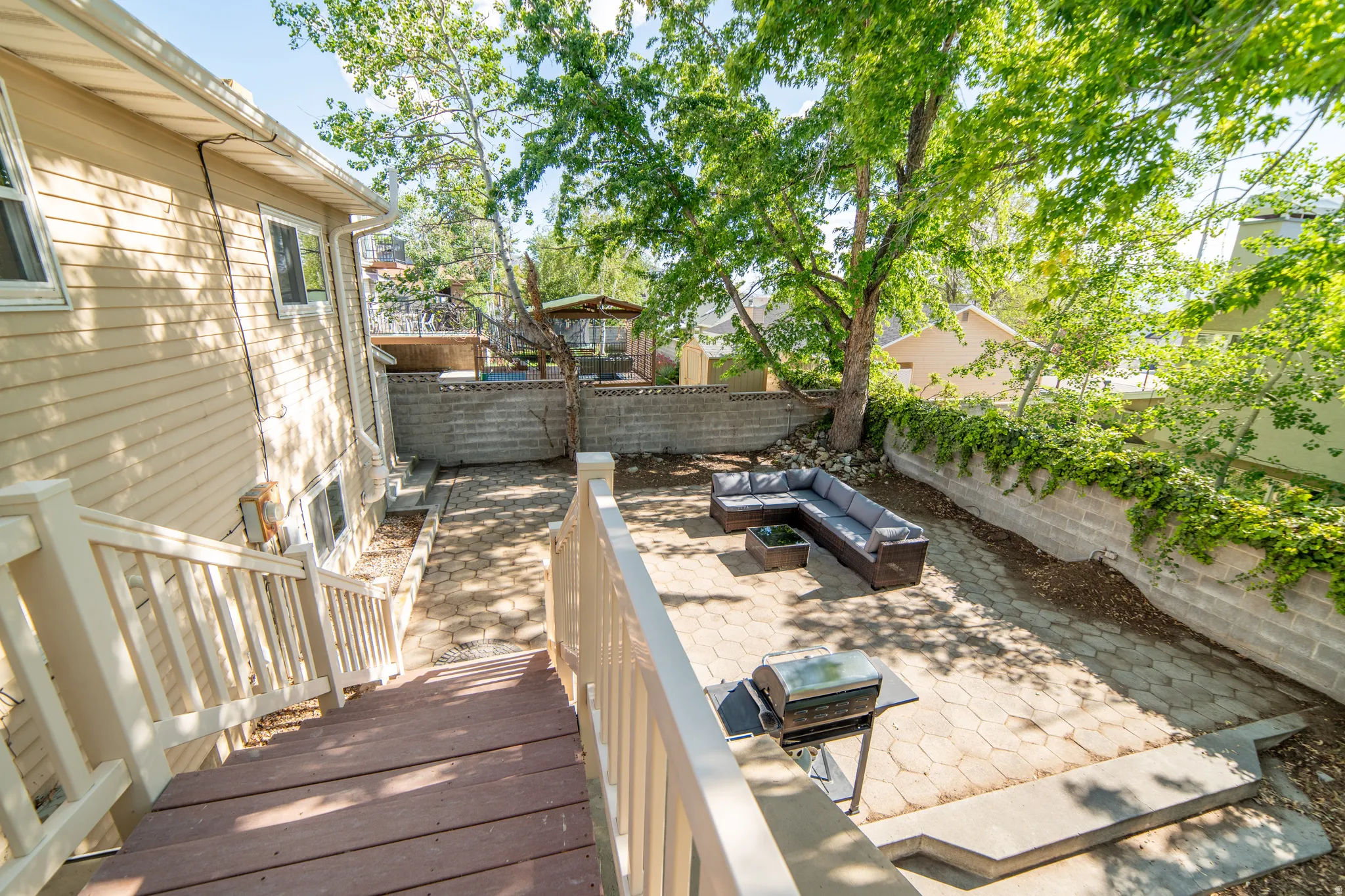 Expansive backyard featuring a multi-level paver patio, a wood-finish deck with white railings, and mature trees providing natural shade