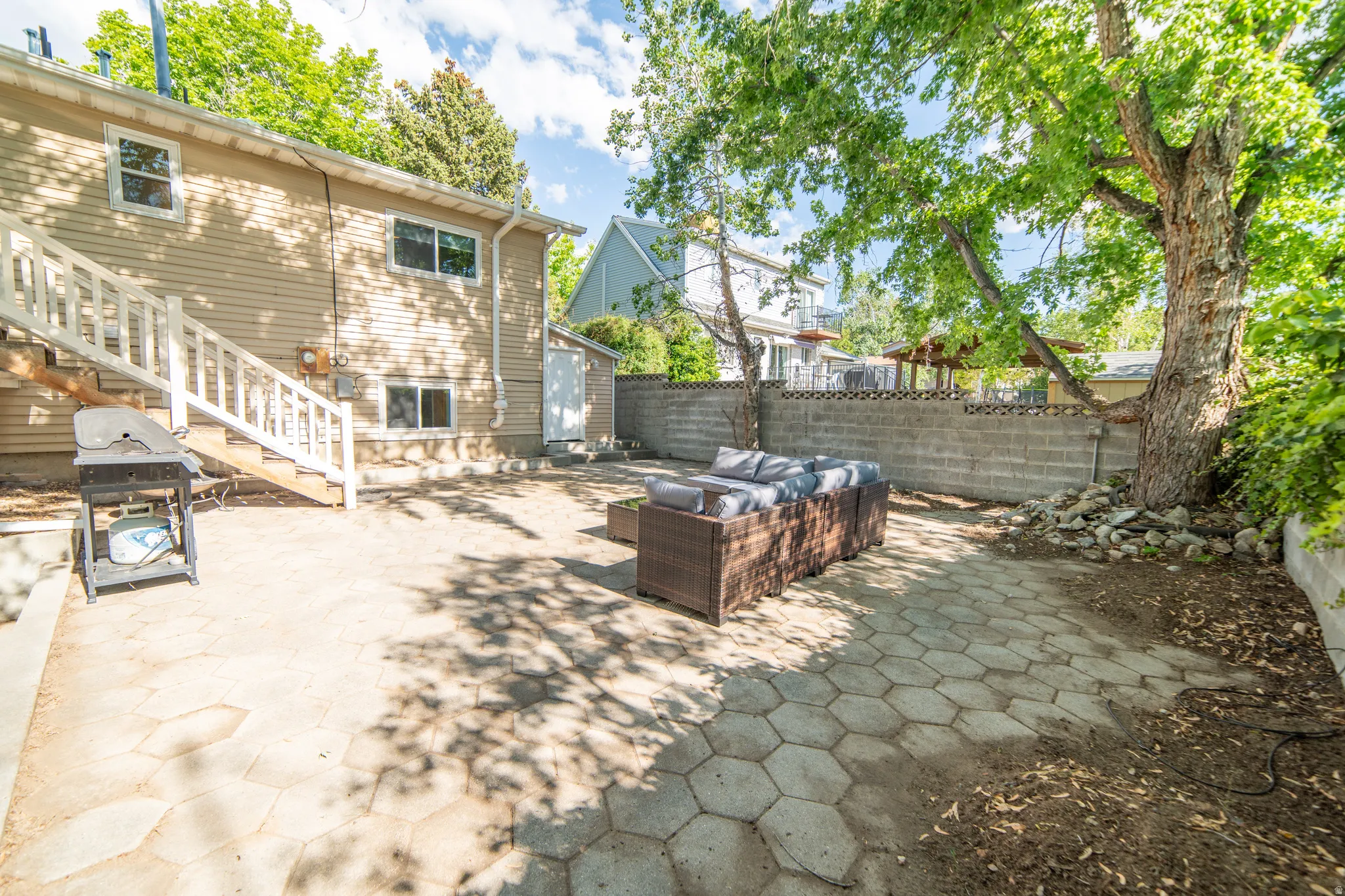 Expansive backyard featuring hexagonal paver patio, mature trees, a privacy wall, and exterior access to the residence