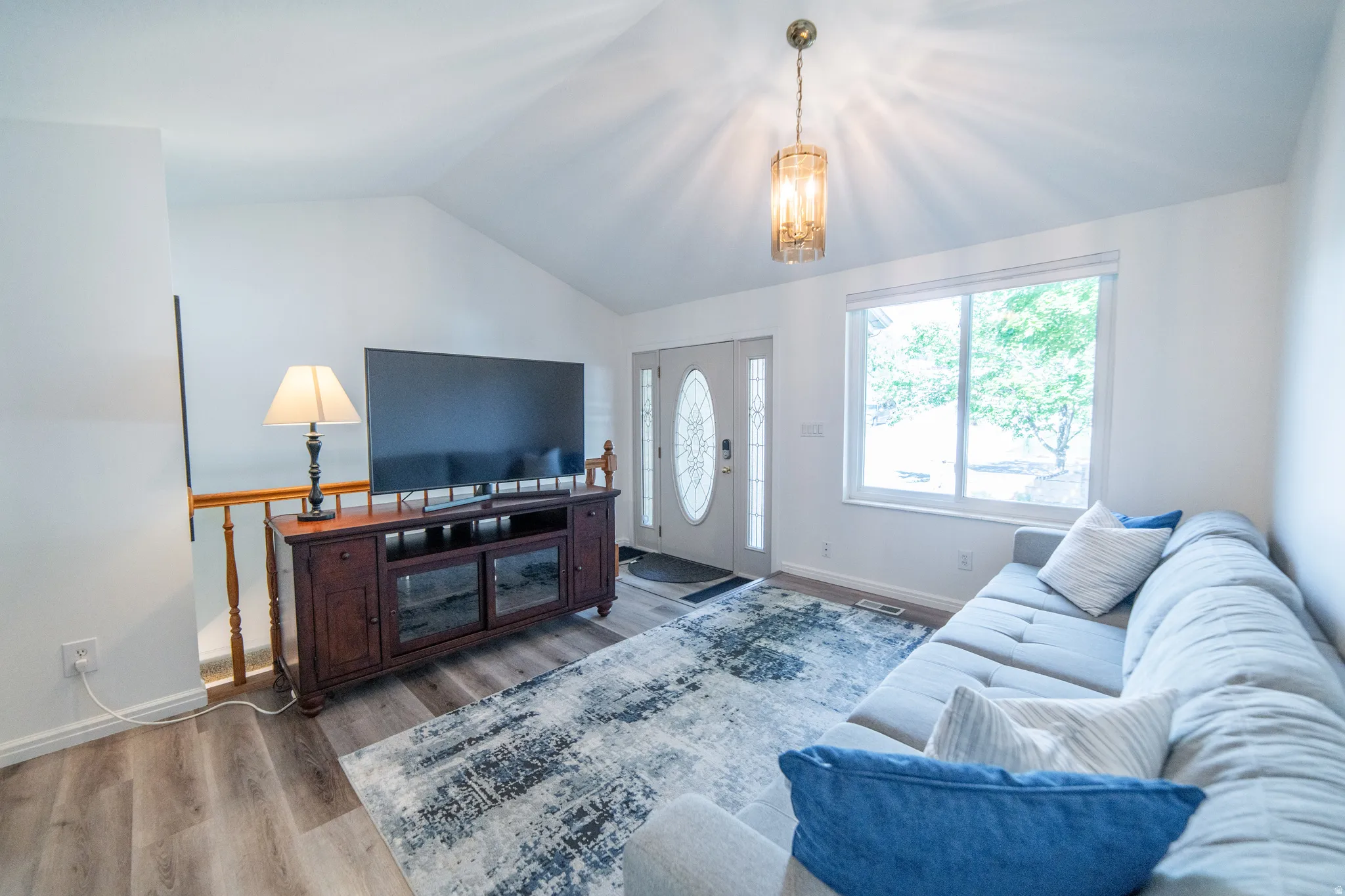 Living area featuring a vaulted ceiling with a decorative pendant light fixture, wood-finish flooring, a bright window, and a glass-paneled entry door