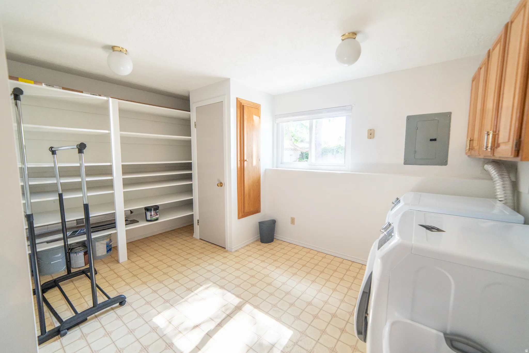 Utility room featuring ample built-in shelving, durable vinyl flooring, a bright window, overhead lighting, and wood-finish cabinetry