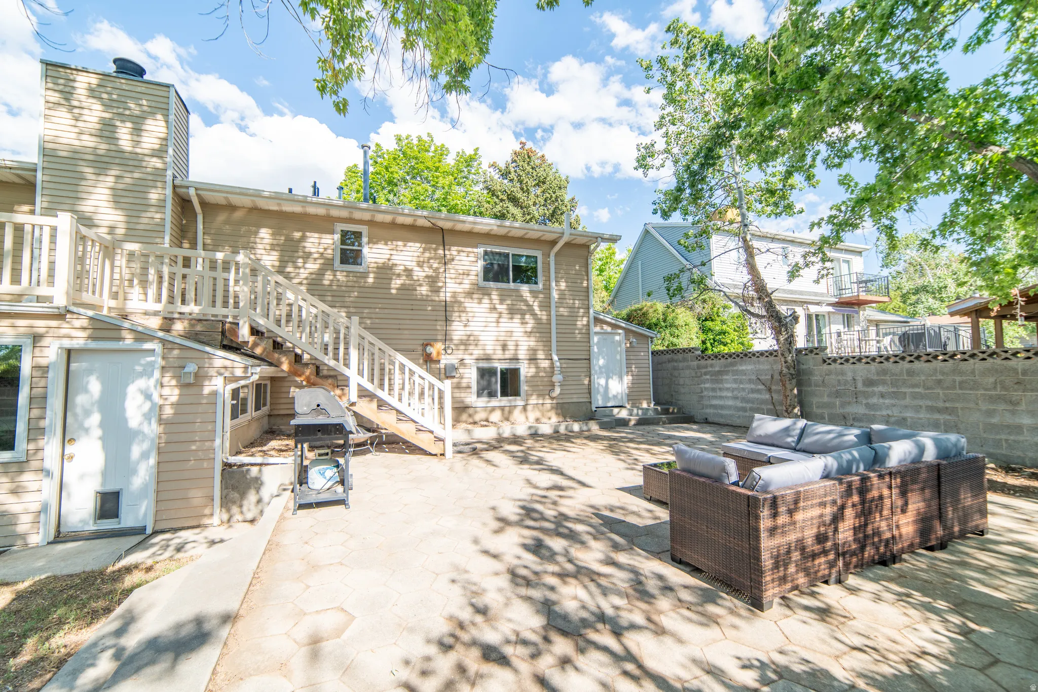 Expansive paved patio area featuring a privacy wall, mature trees, and direct exterior access