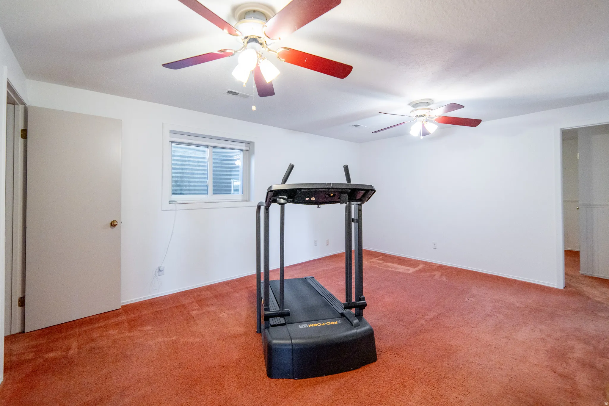 Spacious room featuring neutral white walls and red-hued carpeting