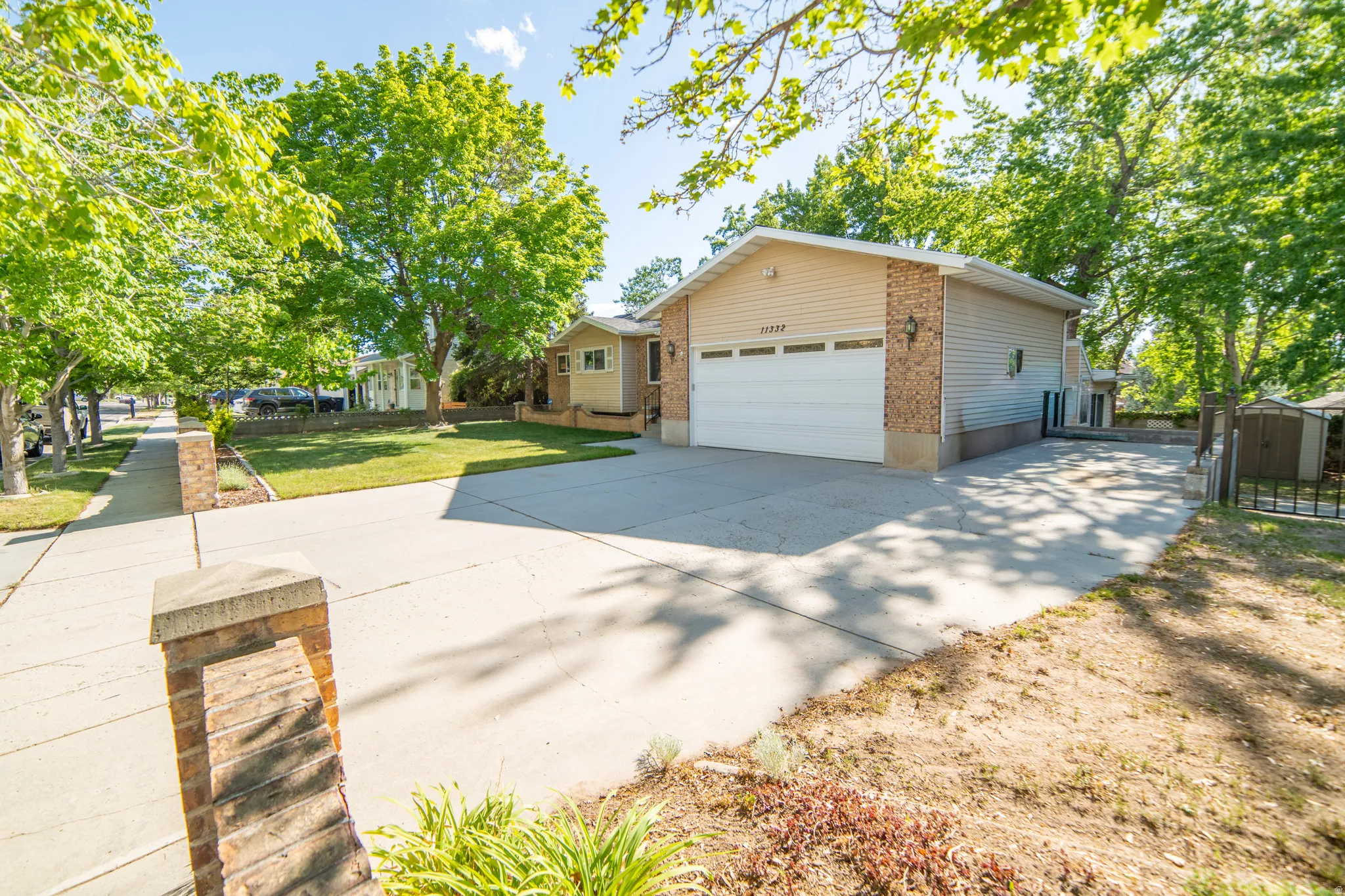 Two-car garage with white door and brick facade, concrete driveway, sidewalk, and mature trees