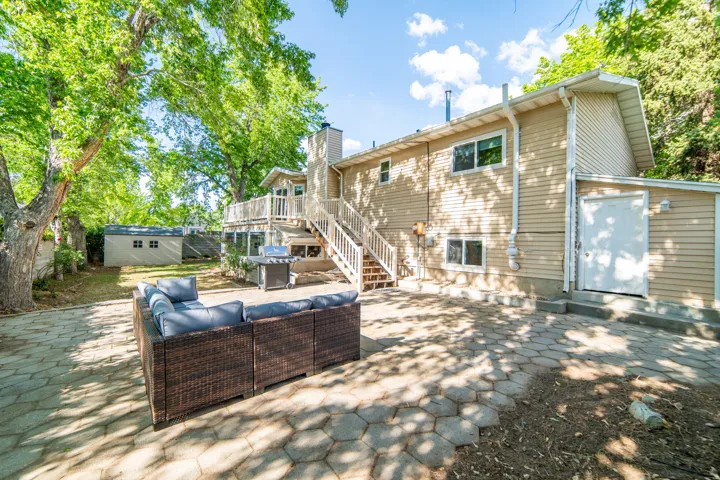 Rear exterior featuring a multi-level deck, lower patio with paver stones, and a detached storage shed