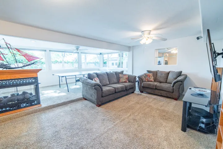 Carpeted living area featuring a fireplace with an oak mantel, a ceiling fan, and large windows providing ample natural light