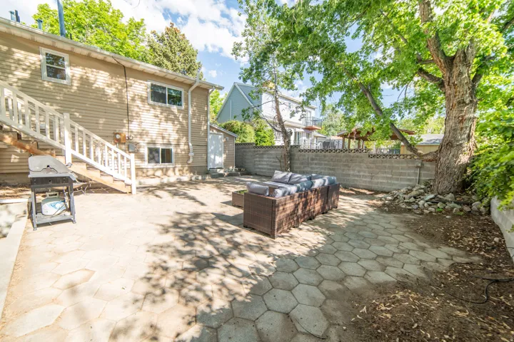 Expansive backyard featuring hexagonal paver patio, mature trees, a privacy wall, and exterior access to the residence