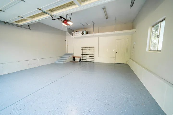 Spacious garage featuring a durable epoxy-coated floor, automatic garage door opener, overhead fluorescent lighting, and integrated storage shelving