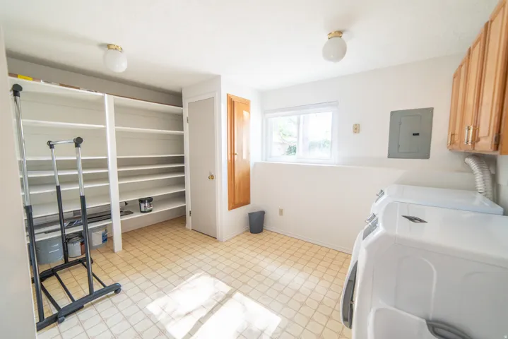 Utility room featuring ample built-in shelving, durable vinyl flooring, a bright window, overhead lighting, and wood-finish cabinetry