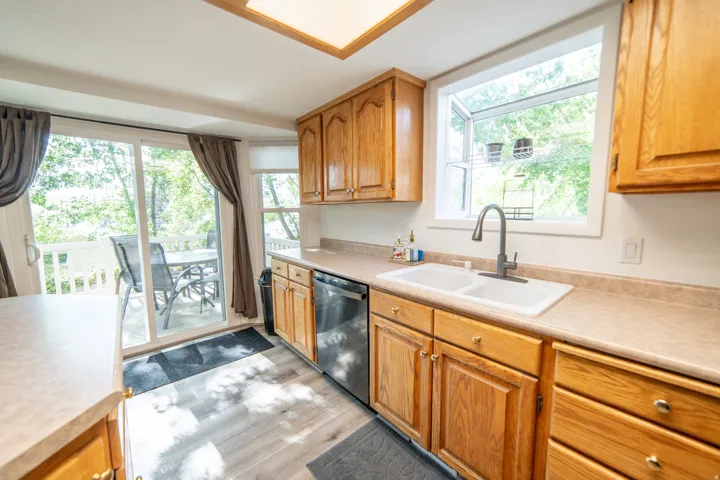 Kitchen featuring wood-finish cabinetry, a double basin sink with a gooseneck faucet, light-toned countertops, and wood-finish flooring