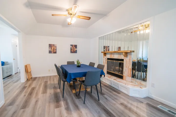 Spacious interior featuring wood-finish flooring, a tray ceiling with a ceiling fan, and a fireplace with a light-toned stone surround and wood mantel