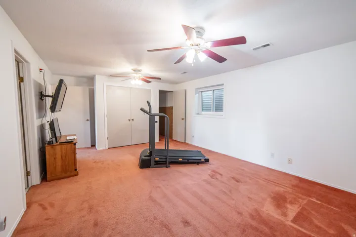 Spacious room featuring neutral white walls, a single horizontal window with blinds, and two ceiling fans with integrated lighting