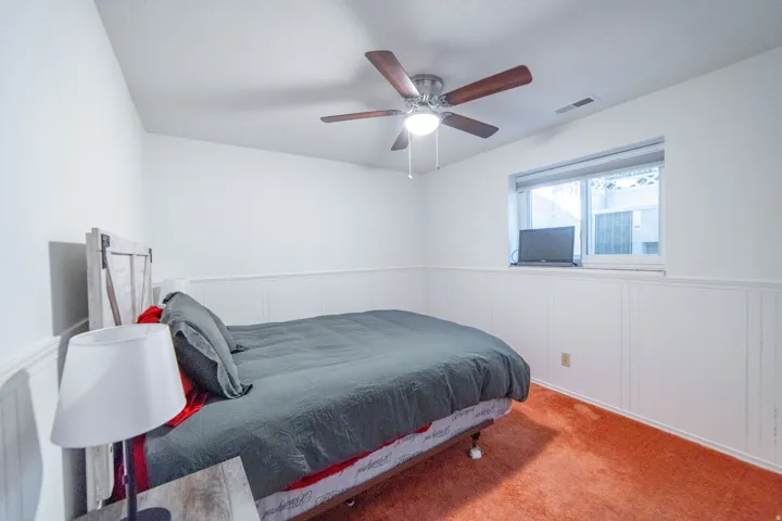 Room featuring white walls with wainscoting, a ceiling fan with light fixture, and a window with a valance
