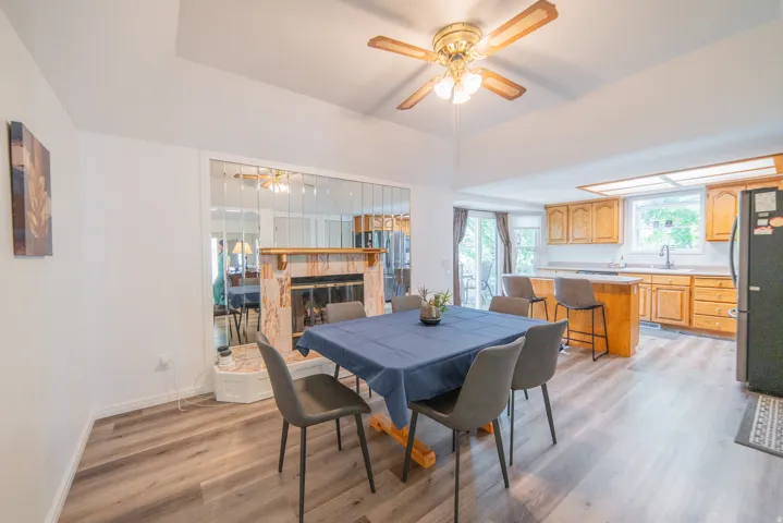 Open-concept living space featuring wood-finish flooring, a tray ceiling with a brass-finish ceiling fan, and a fireplace with a decorative mantel and mirrored surround