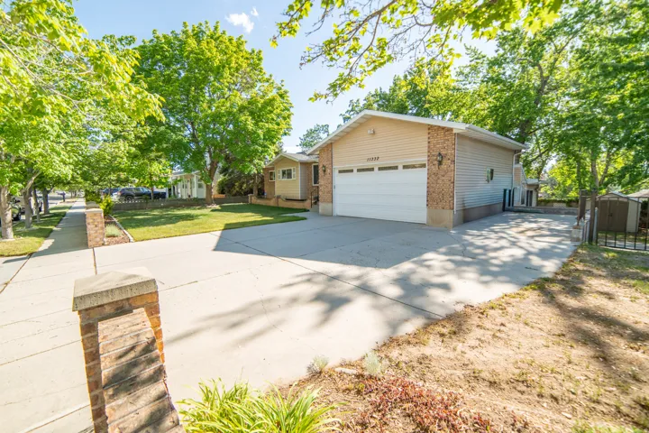 Two-car garage with white door and brick facade, concrete driveway, sidewalk, and mature trees