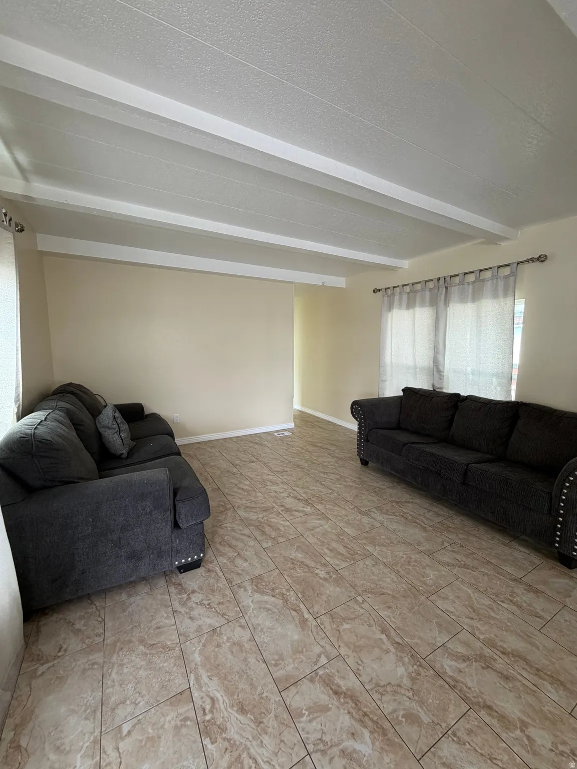 Spacious living area featuring exposed white ceiling beams and light-toned tile flooring