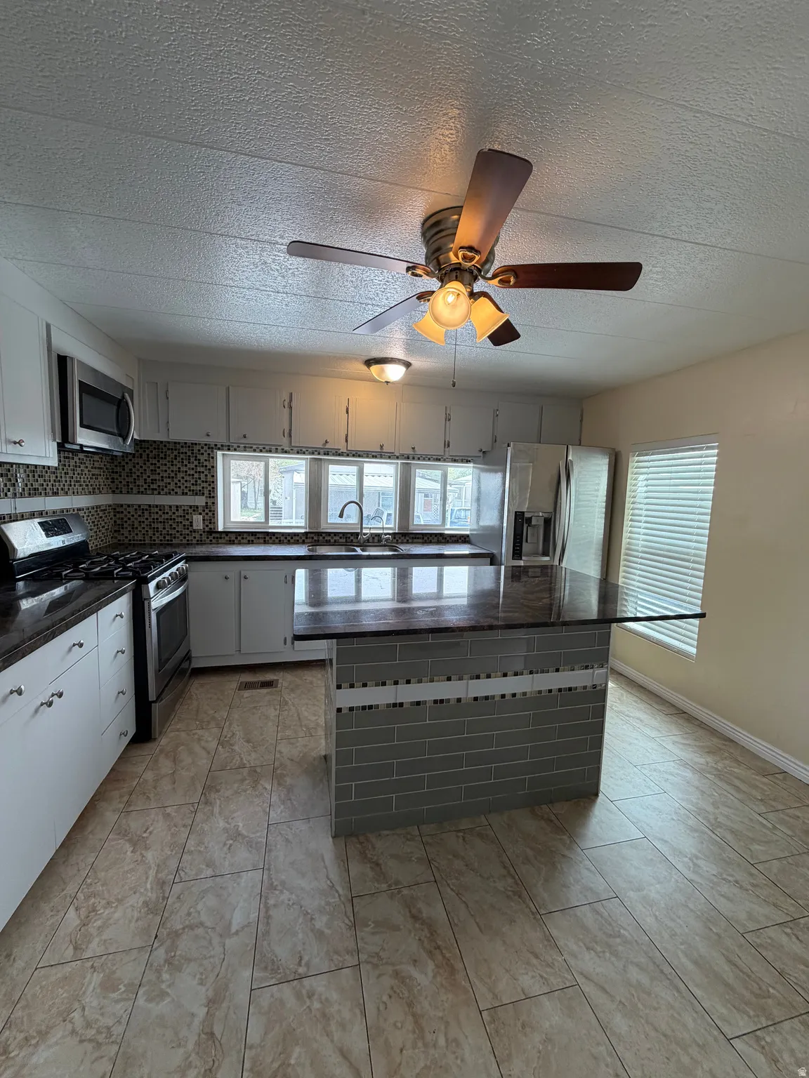 Kitchen featuring a tiled floor, dark countertops, white cabinetry, stainless steel appliances, and a tiled island with seating