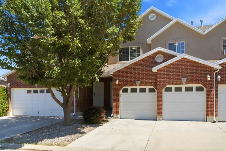 Brick exterior with white garage doors and a mature tree