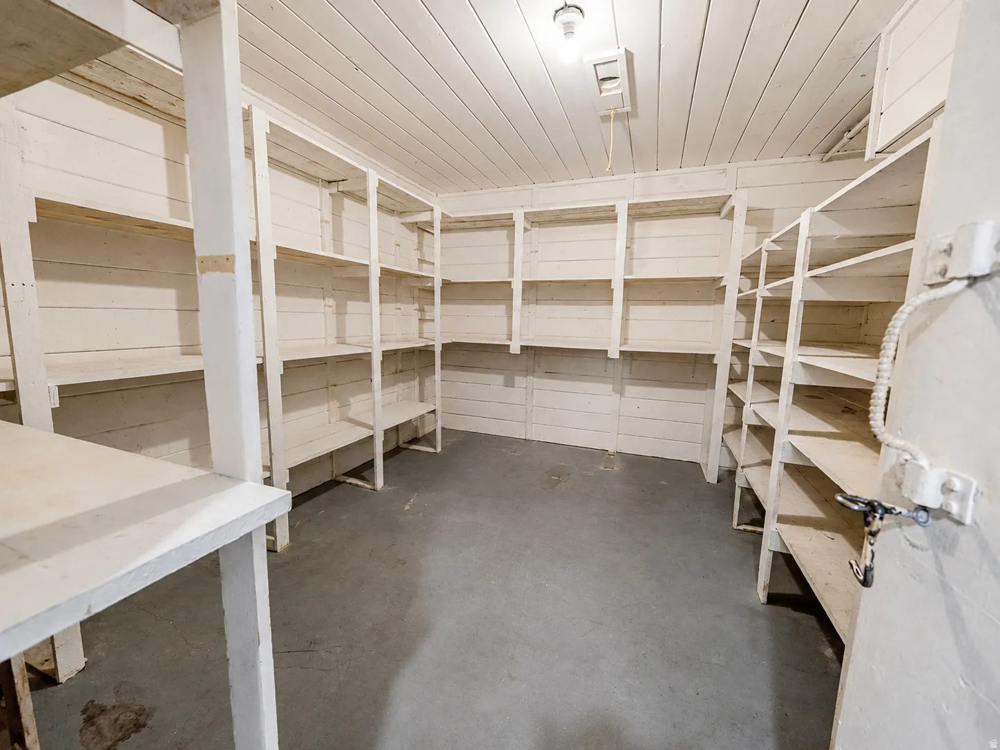 Dedicated storage room featuring multiple built-in shelving units, painted wood paneling, and a concrete floor
