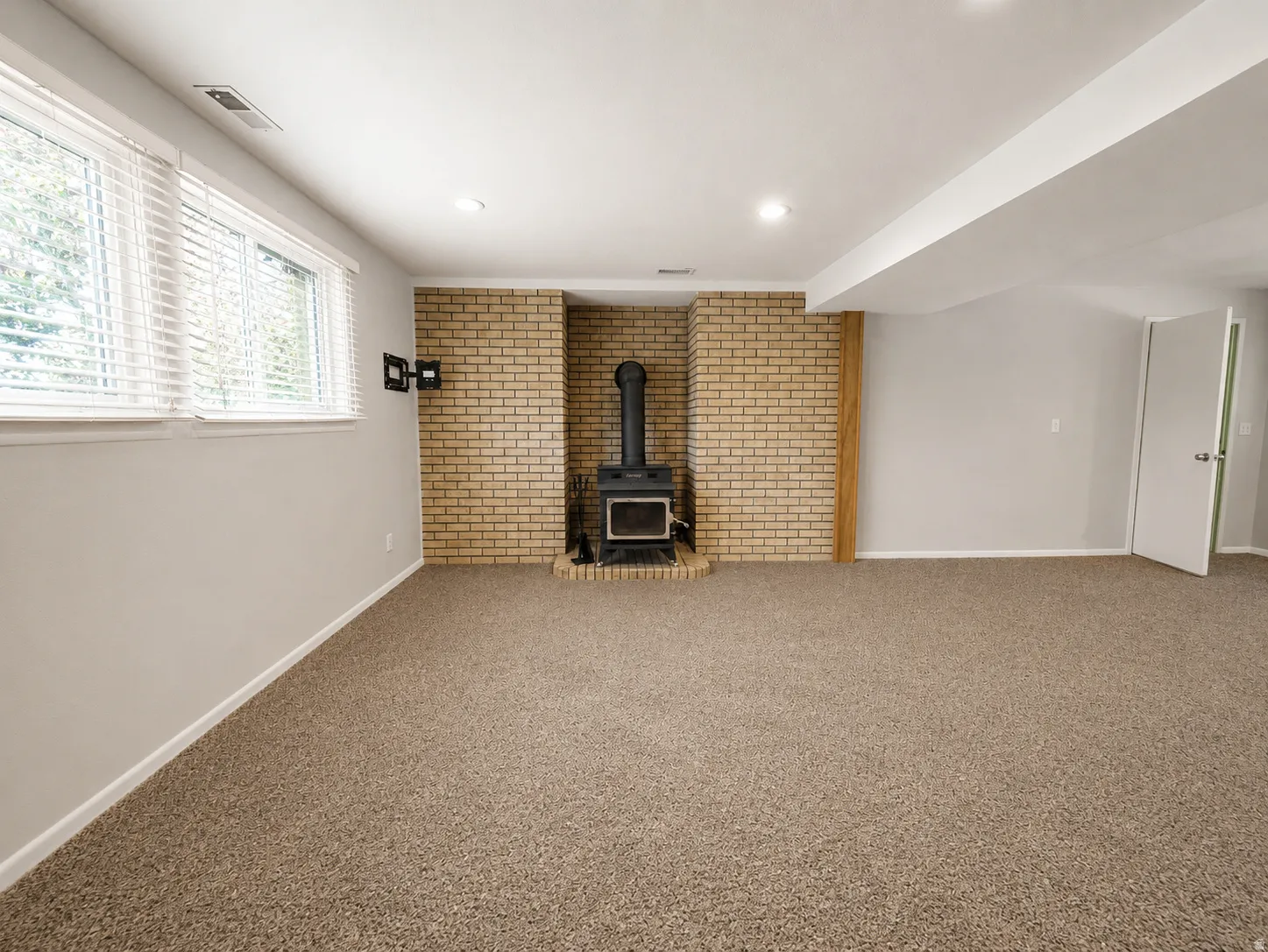 Spacious room featuring a brick-clad wood stove, multiple windows with blinds, light gray wall paint, and recessed ceiling lighting