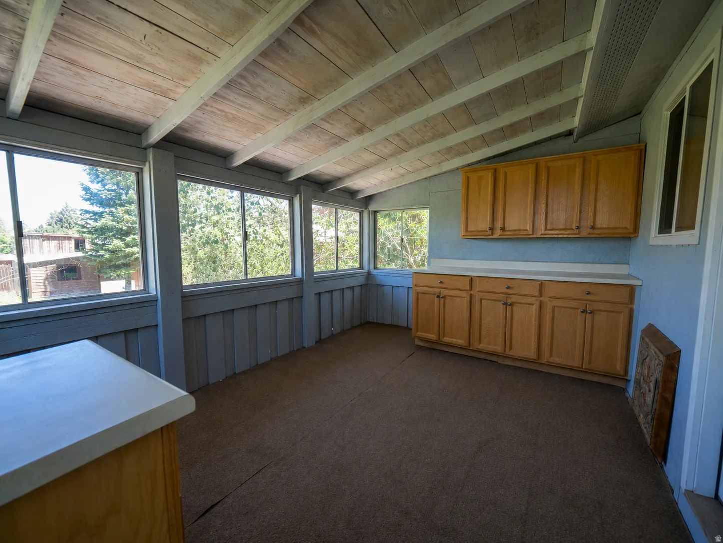 Enclosed porch featuring multiple large windows, wood-finish cabinetry with light countertops, and a wood plank ceiling