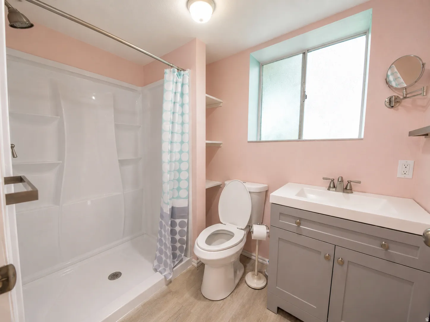 Bathroom featuring a white shower stall, a single-pane window with frosted glass, a toilet, a gray vanity with an integrated sink, and wood-finish flooring