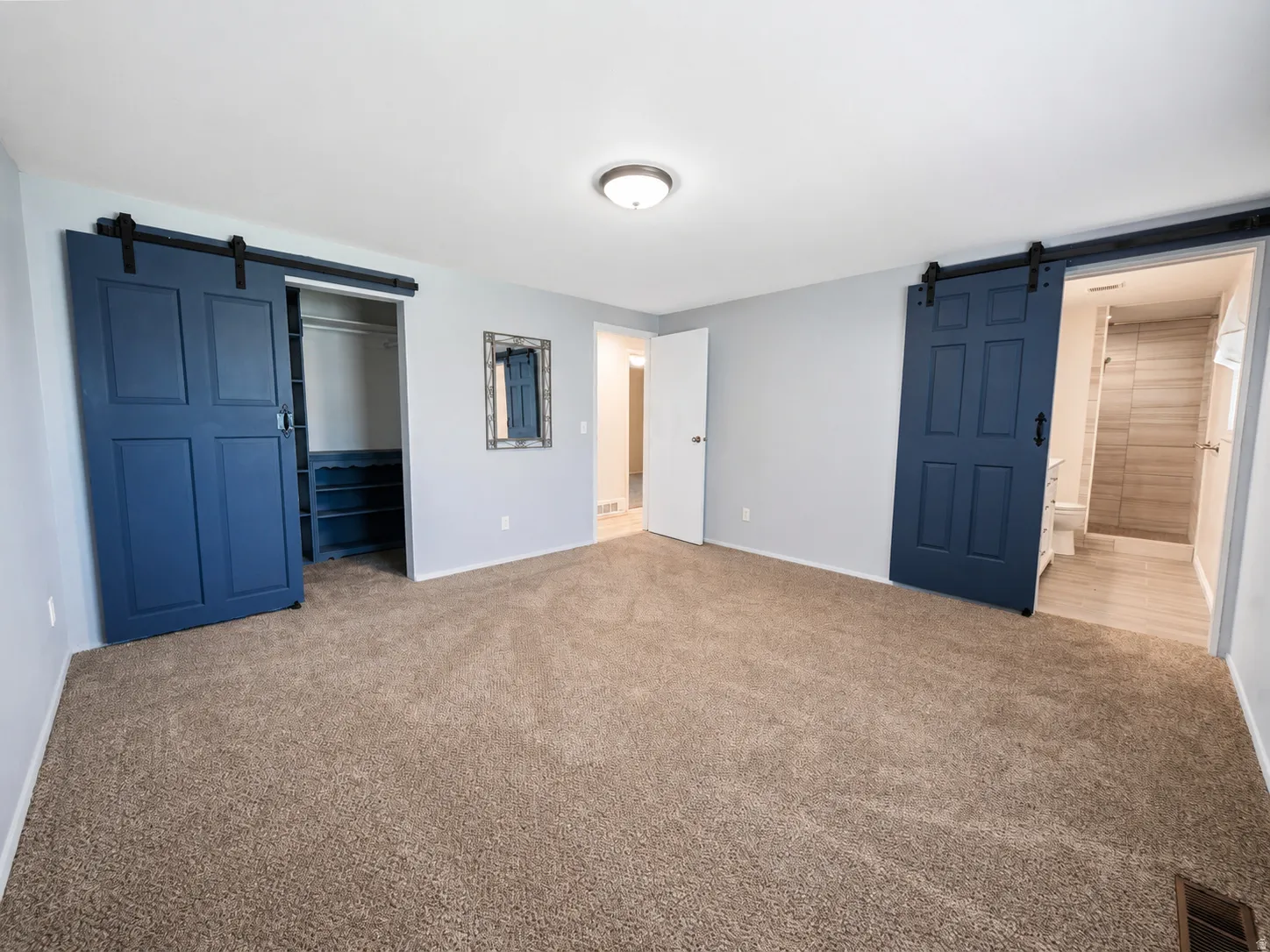Spacious room featuring plush carpet flooring, two blue barn doors, a recessed ceiling light fixture, and an entry to a bathroom with tiled walls and flooring