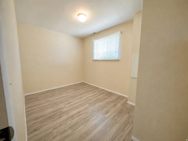 Room featuring wood-finish flooring, a neutral wall palette, a single window with horizontal blinds, and an overhead flush-mount light fixture