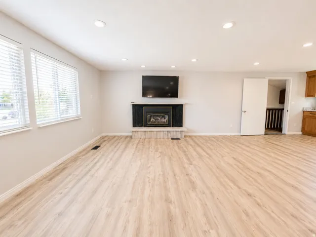 Spacious room featuring wood-finish flooring, recessed ceiling lighting, a fireplace with a black surround and stone hearth, and multiple windows with blinds