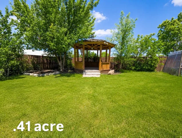 Expansive lawn featuring a wooden gazebo with steps, mature trees, and a privacy fence