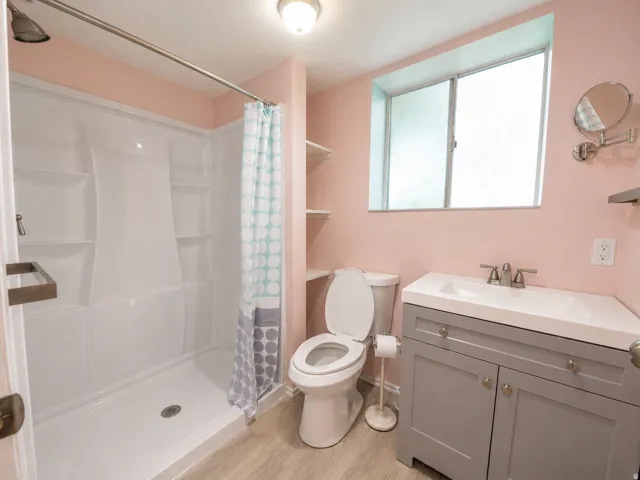 Bathroom featuring a white shower stall, a single-pane window with frosted glass, a toilet, a gray vanity with an integrated sink, and wood-finish flooring