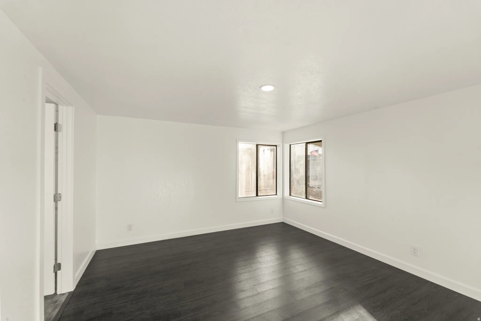 Spacious room featuring dark wood-finish flooring, white walls, and a recessed ceiling light