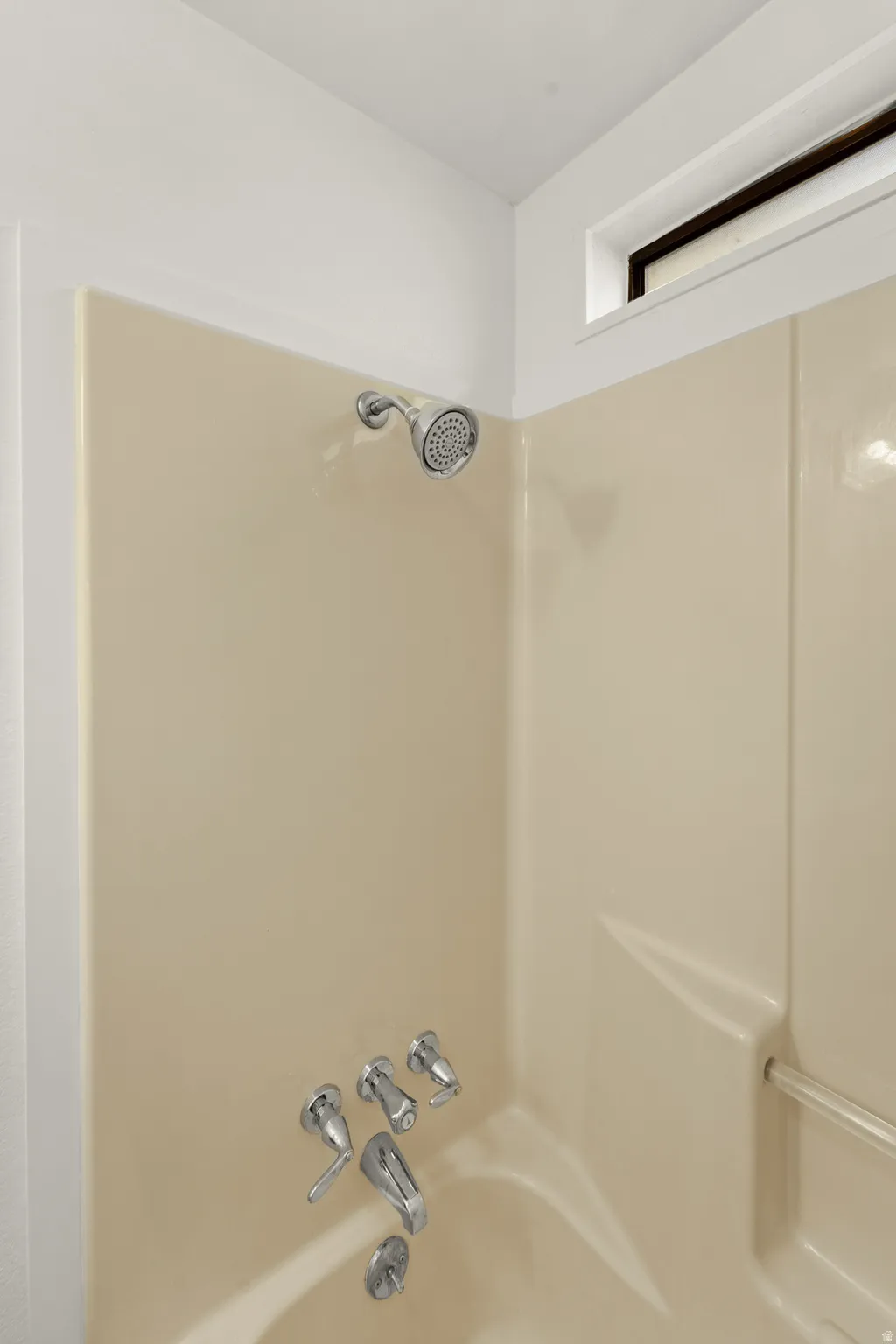 Bathtub with a cream-toned surround, chrome showerhead, and matching fixtures