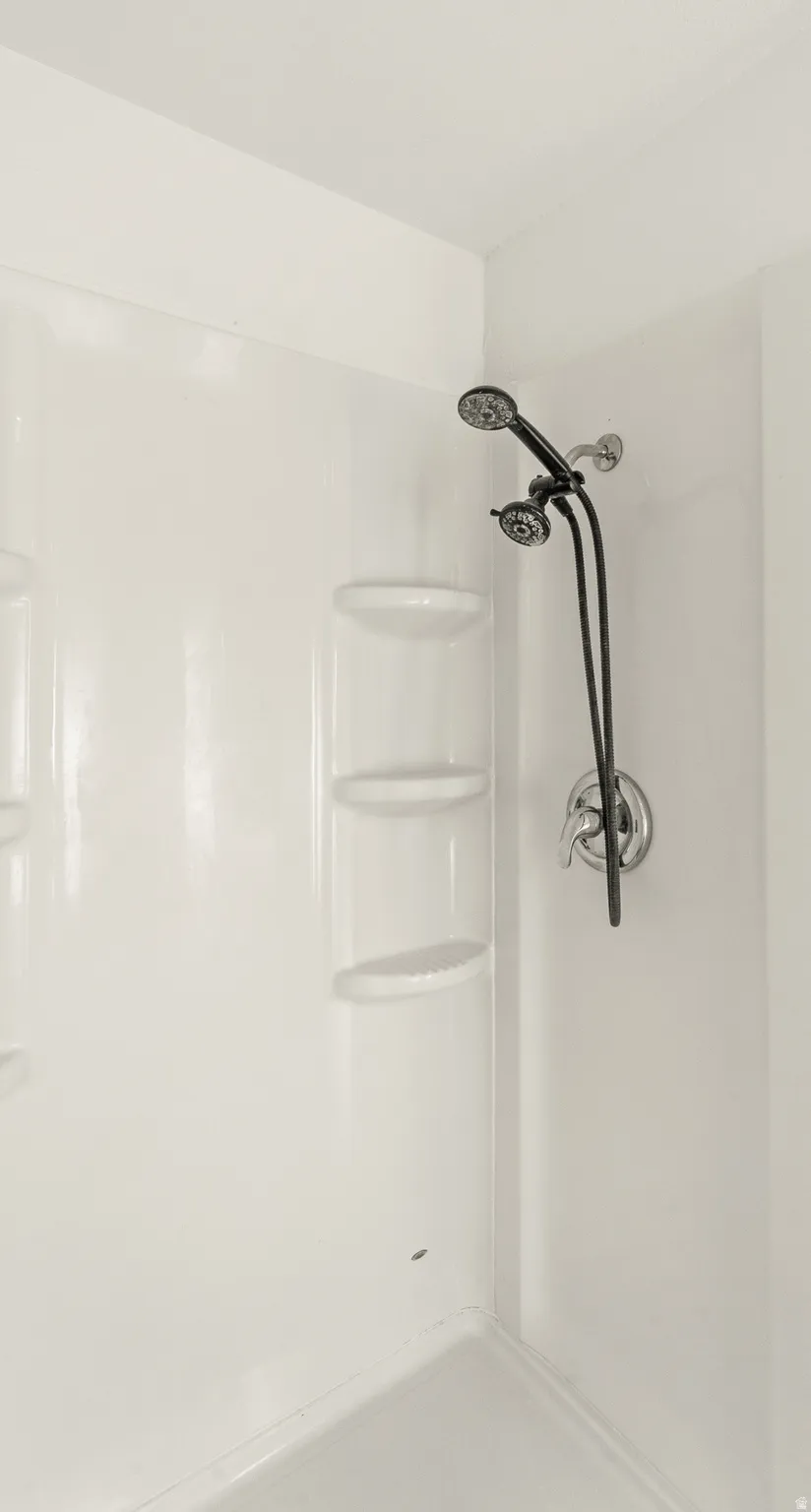 White shower surround with built-in corner shelving and a dual shower head fixture