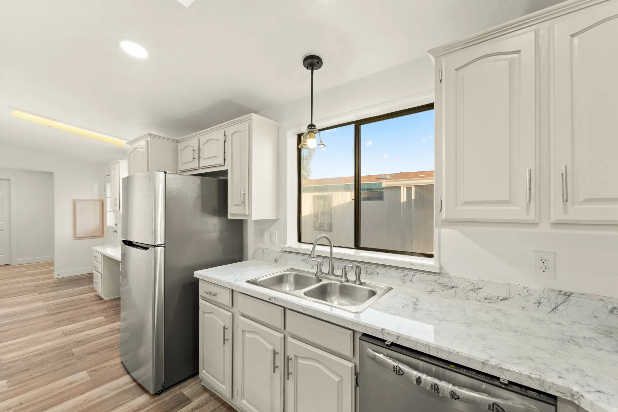 Kitchen featuring light wood-finish flooring, white cabinetry, stainless steel appliances, and a double basin sink