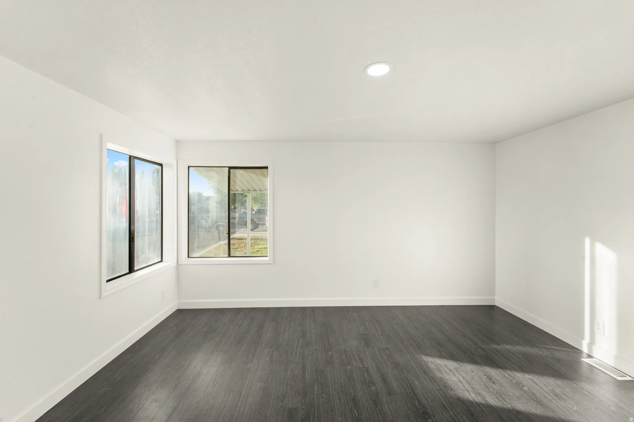 Spacious room featuring dark wood-finish flooring, white baseboards, and two large windows with white trim