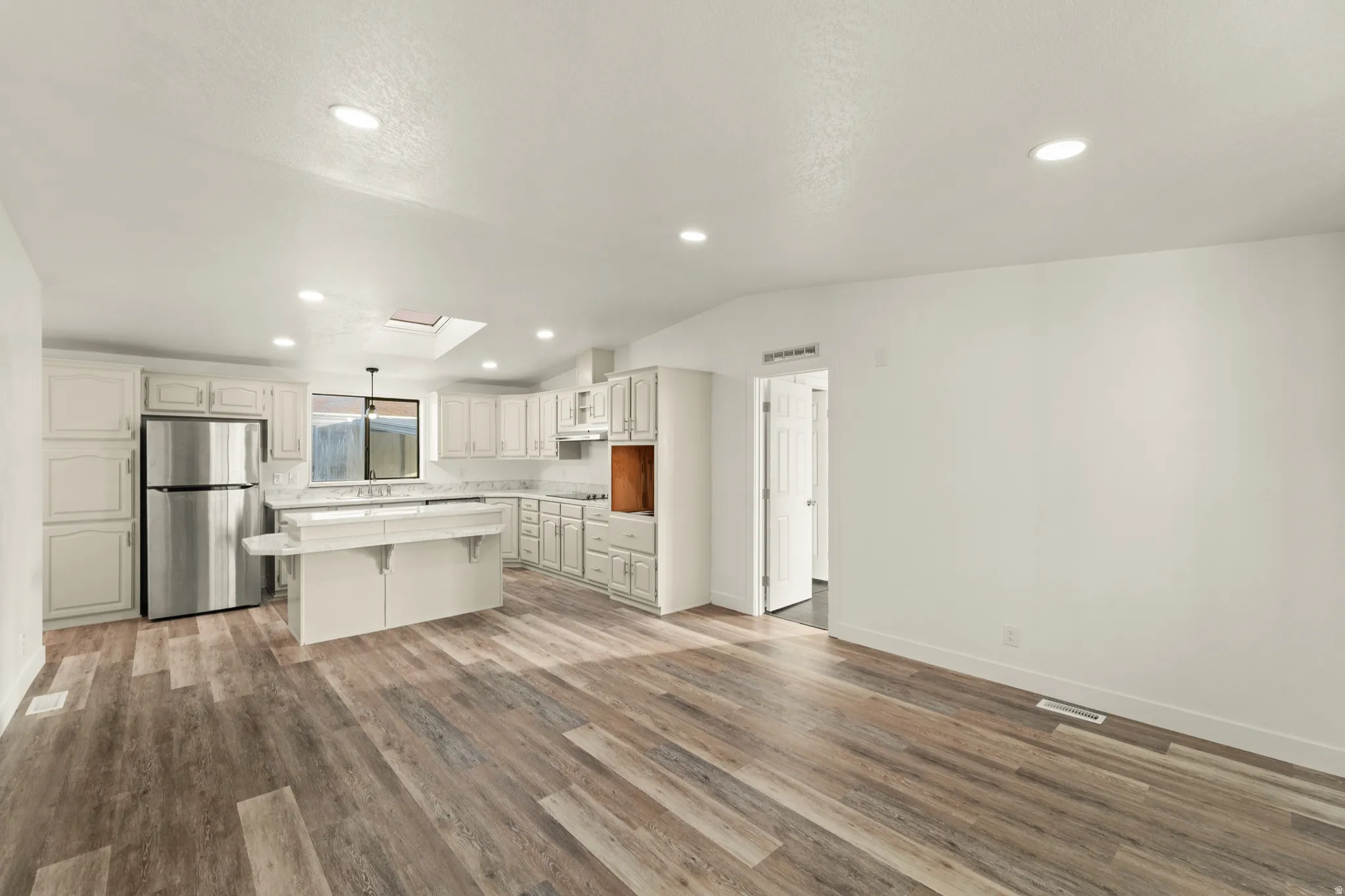 Open-concept living space featuring wood-finish flooring, recessed lighting, and a skylight