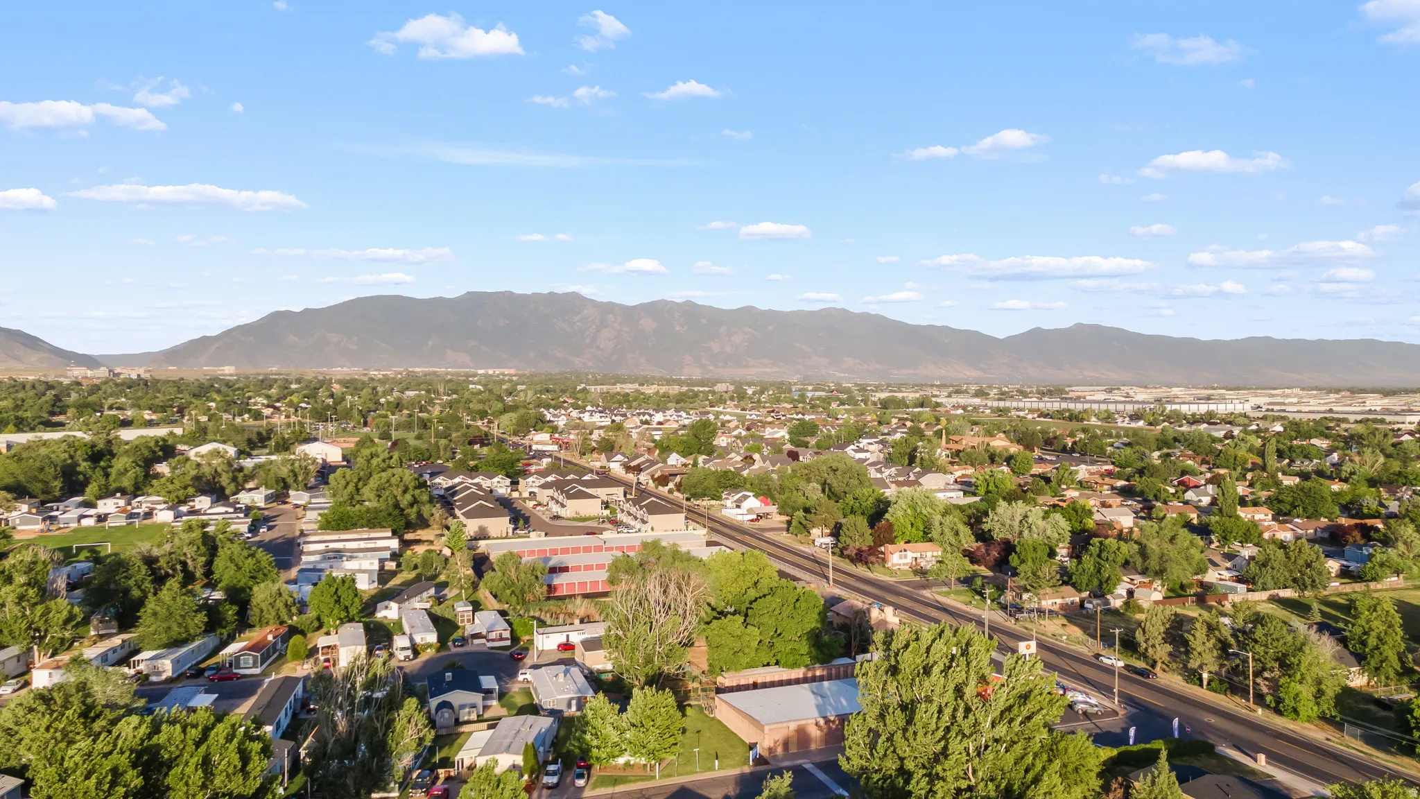Expansive aerial perspective showcasing a residential area with mature tree coverage, a primary roadway, and distant mountain ranges