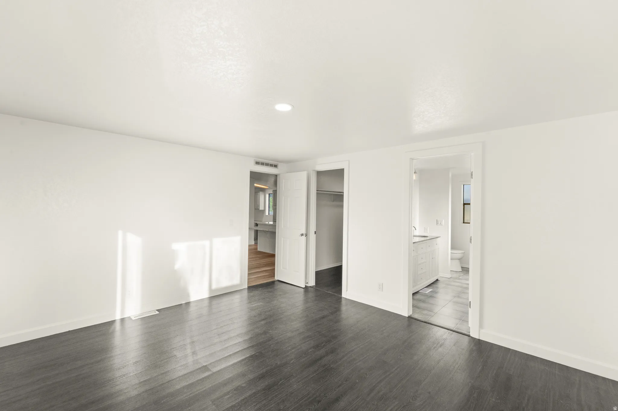 Spacious room featuring dark wood-finish flooring and crisp white walls