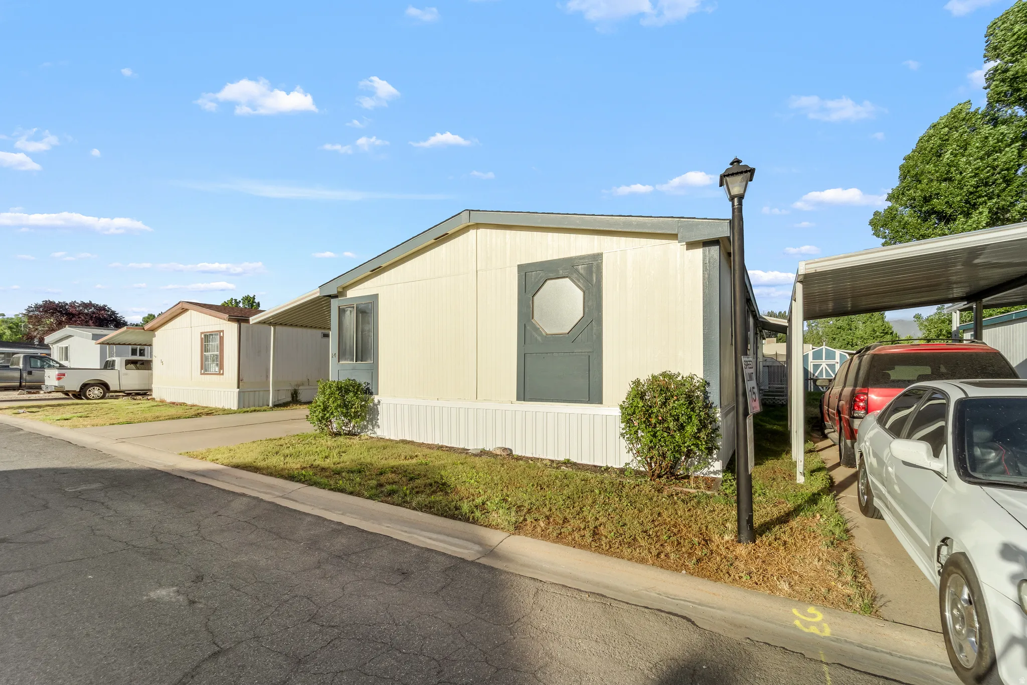 Exterior featuring light-colored siding, a covered carport, a street lamp, and front landscaping