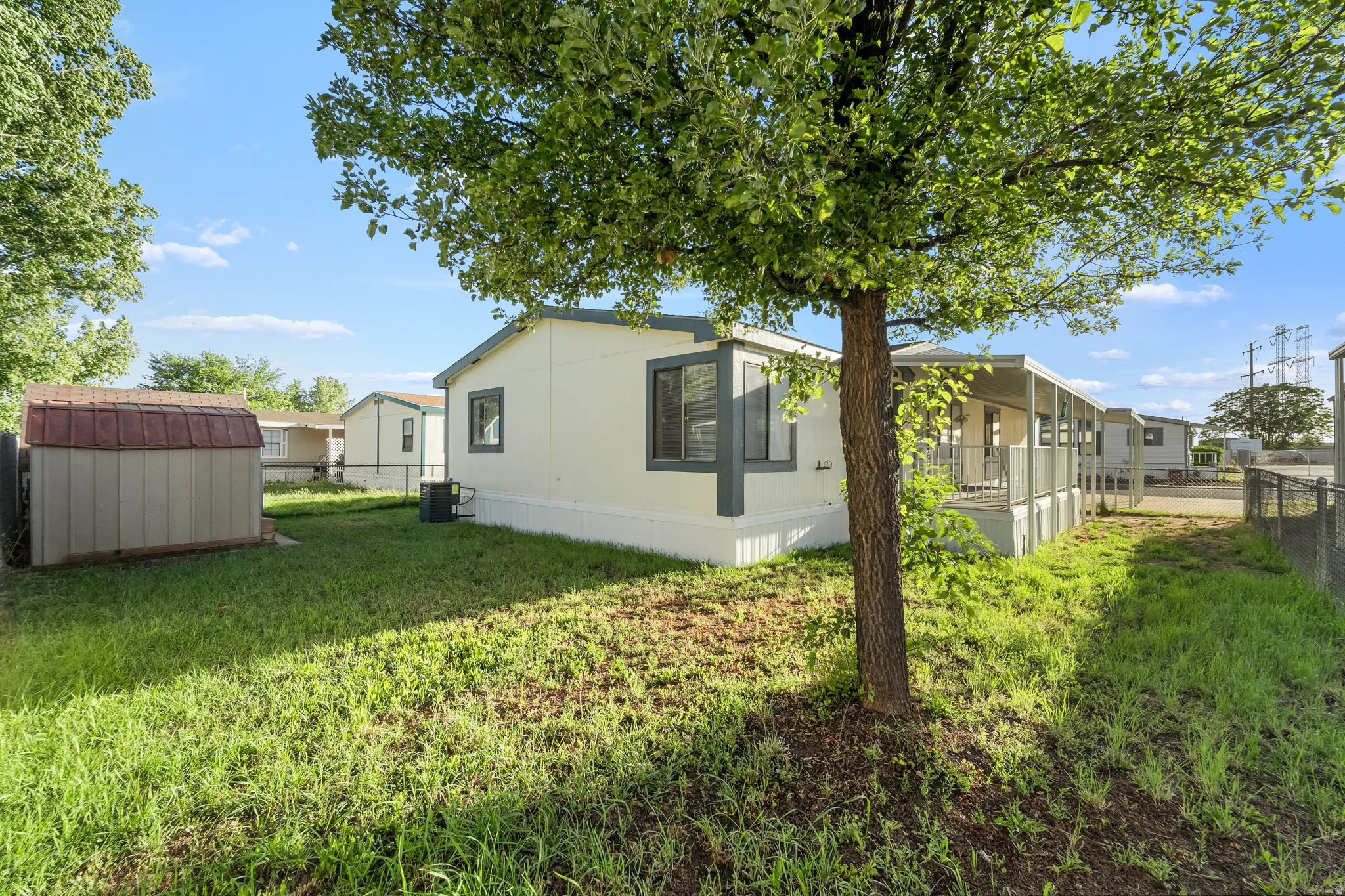 Spacious outdoor area featuring a mature tree, a detached storage shed with a brown roof, and a fenced perimeter