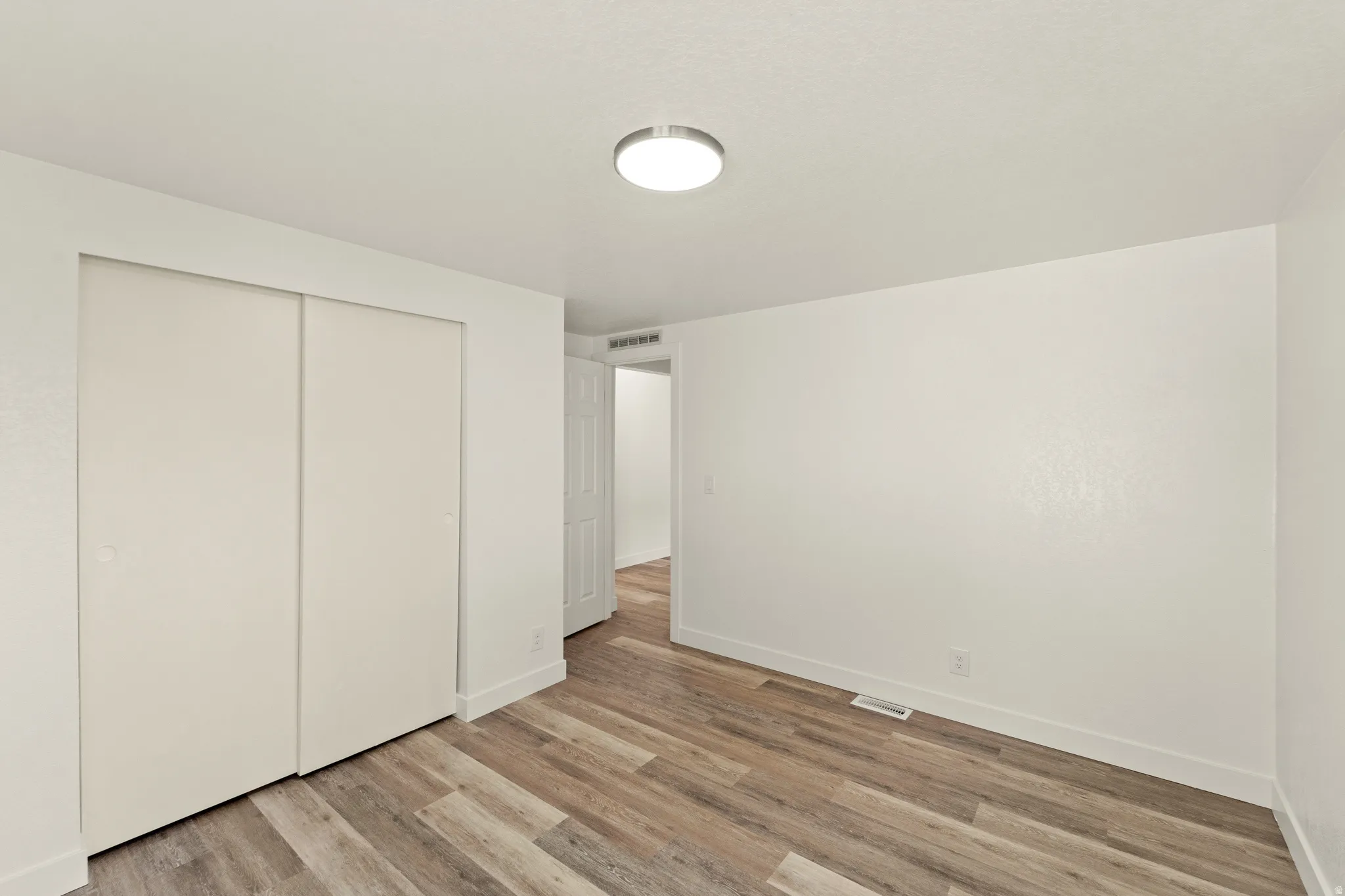 Interior room featuring wood-finish flooring, white baseboards, and a flush-mount ceiling light fixture