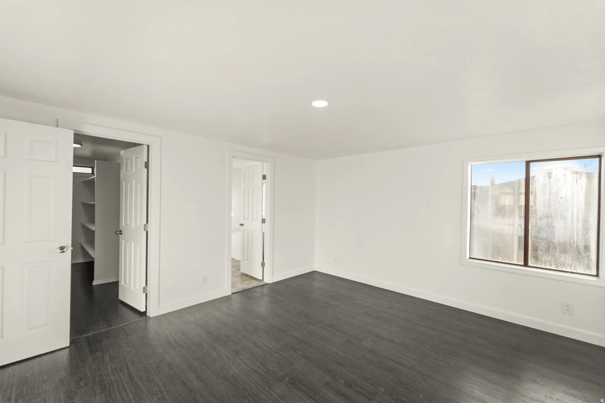 Spacious room featuring dark wood-finish flooring, recessed lighting, and a window with white trim