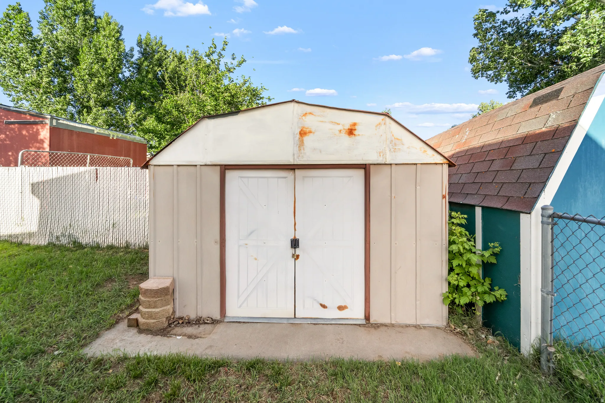 Exterior storage shed with double doors, set on a concrete pad, surrounded by a grassy area