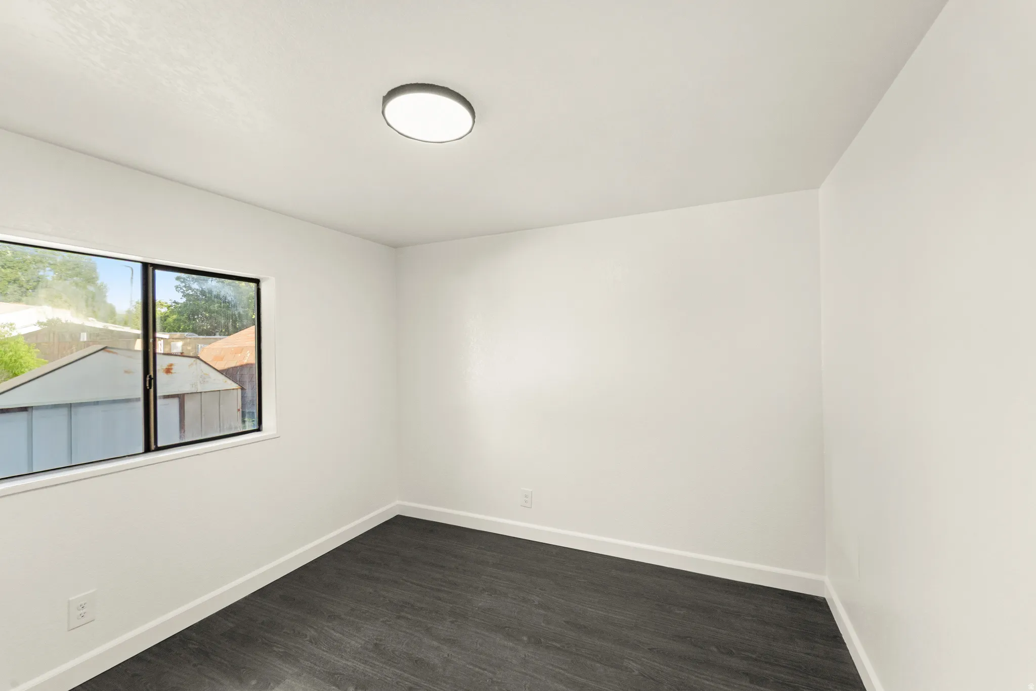 Spacious room featuring wood-finish flooring, crisp white walls, and a large window