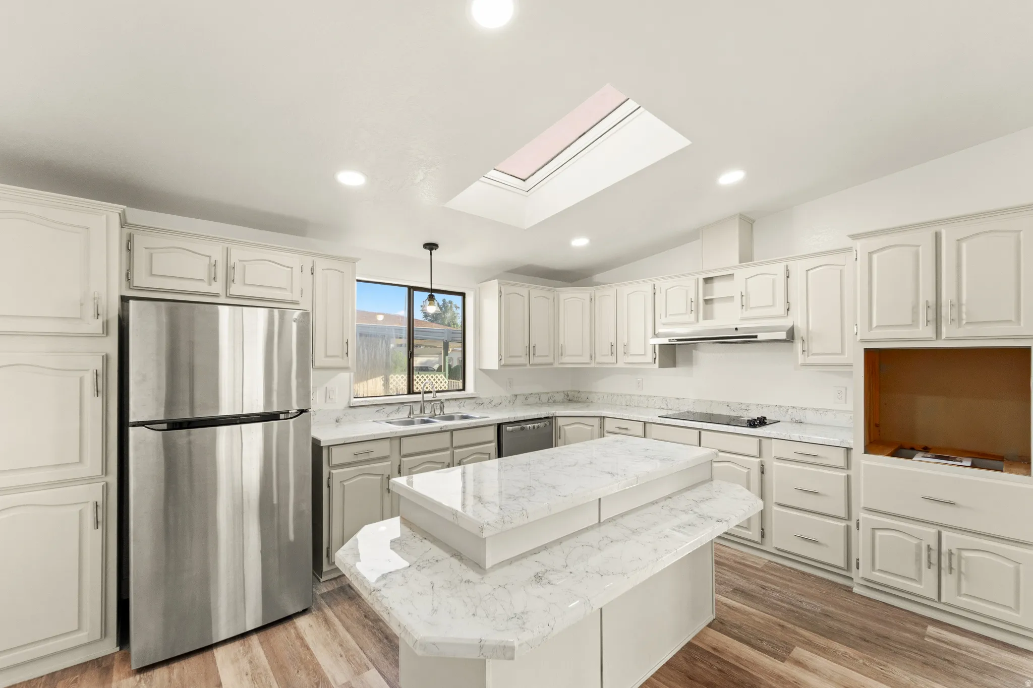 Kitchen featuring a central island with a multi-level countertop, light-toned cabinetry, stainless steel appliances, a skylight, and wood-finish flooring