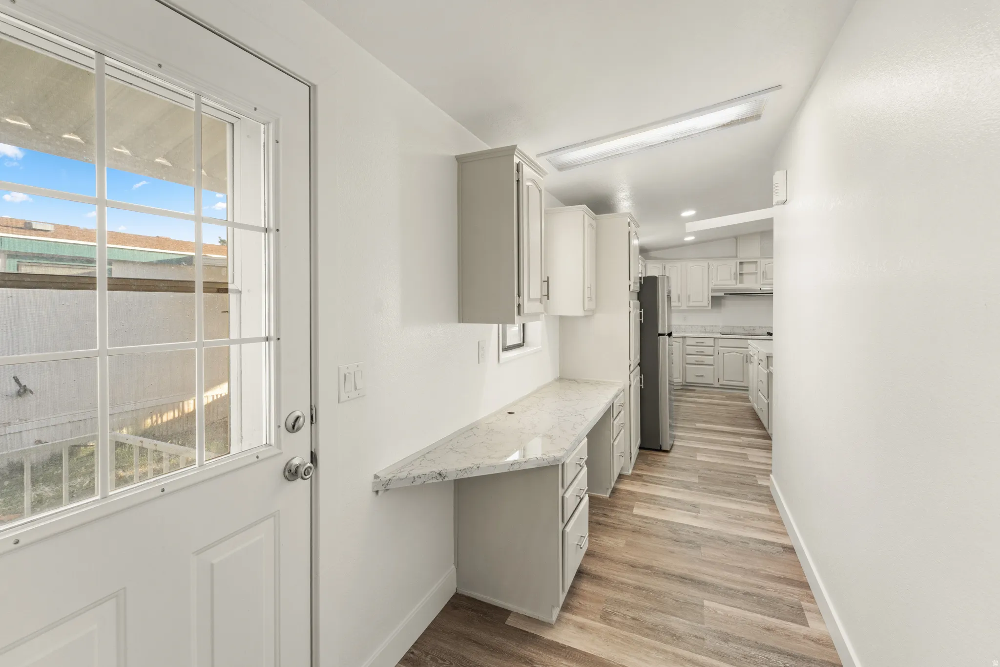 Entryway featuring a white paneled door with glass inserts, wood-finish flooring, a built-in desk with a light-toned countertop, and recessed lighting