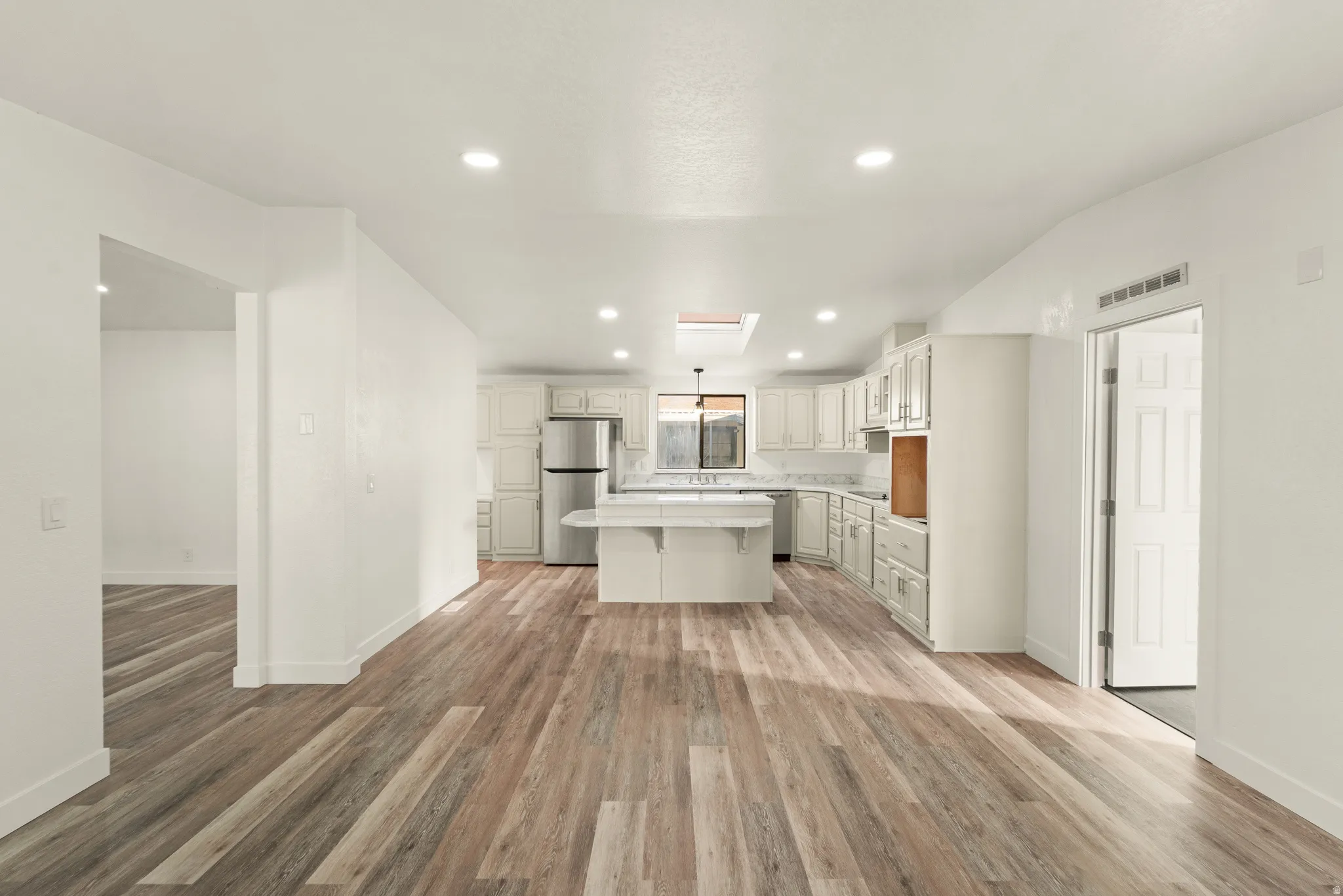 Open-concept kitchen and living area featuring wood-finish flooring, recessed lighting, and a skylight