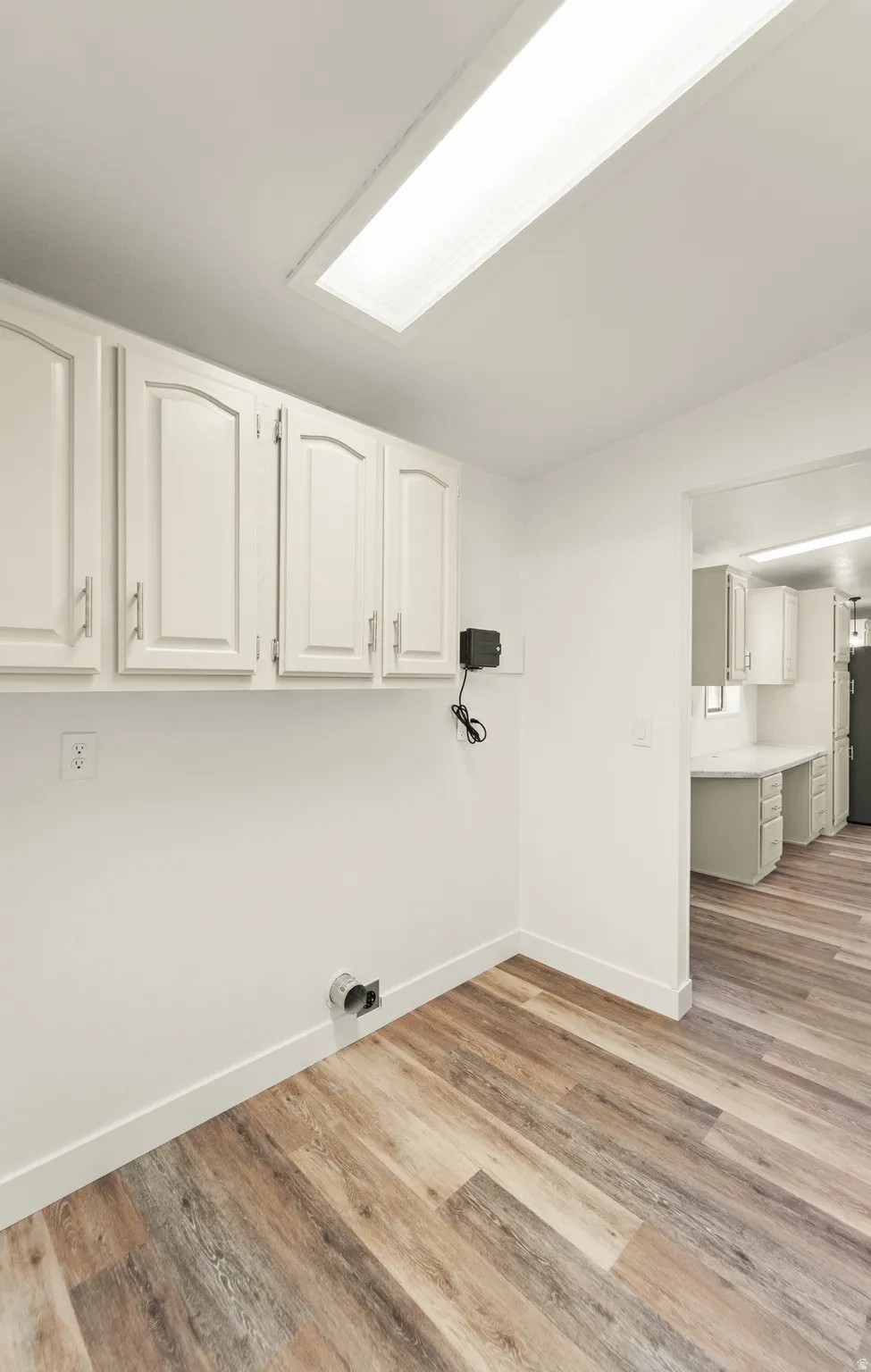 Utility space featuring white cabinetry with brushed nickel hardware, wood-finish flooring, and a rectangular ceiling light fixture