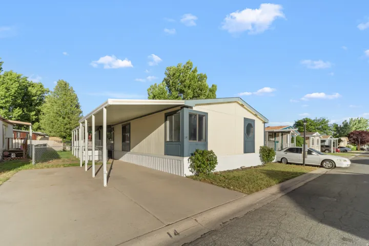 Cream-colored exterior featuring a covered carport, dark blue trim, and established shrubbery